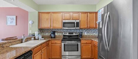 A kitchen with wooden cabinets, a stainless steel refrigerator, a microwave, an oven, and a dishwasher.