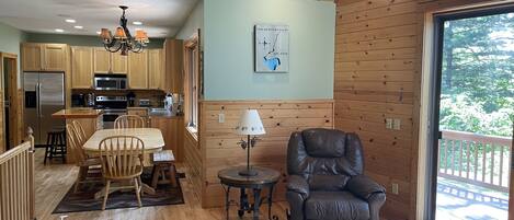 L’intérieur chaleureux d’un chalet avec des murs en bois, un coin repas, une cuisine et une grande fenêtre donnant sur le paysage extérieur.