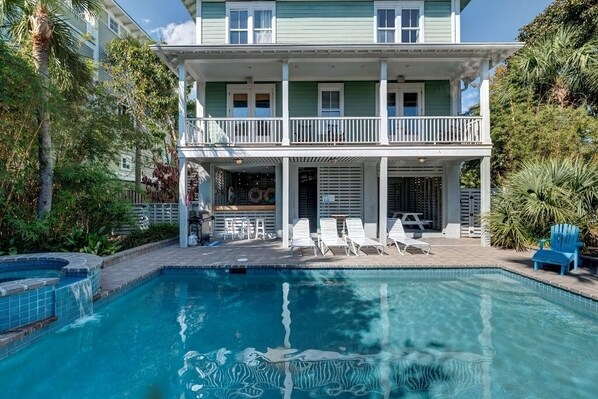 Uma casa de dois andares com piscina, um alpendre coberto com espreguiçadeiras e uma pequena área de deck.