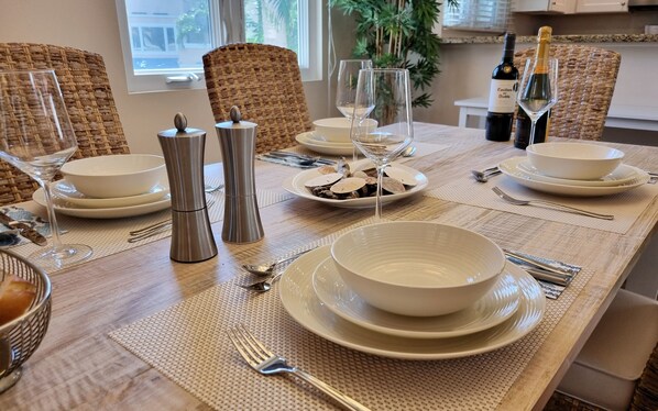 A dining table set with white plates, bowls, and silverware, along with two wine glasses and a bottle of wine.