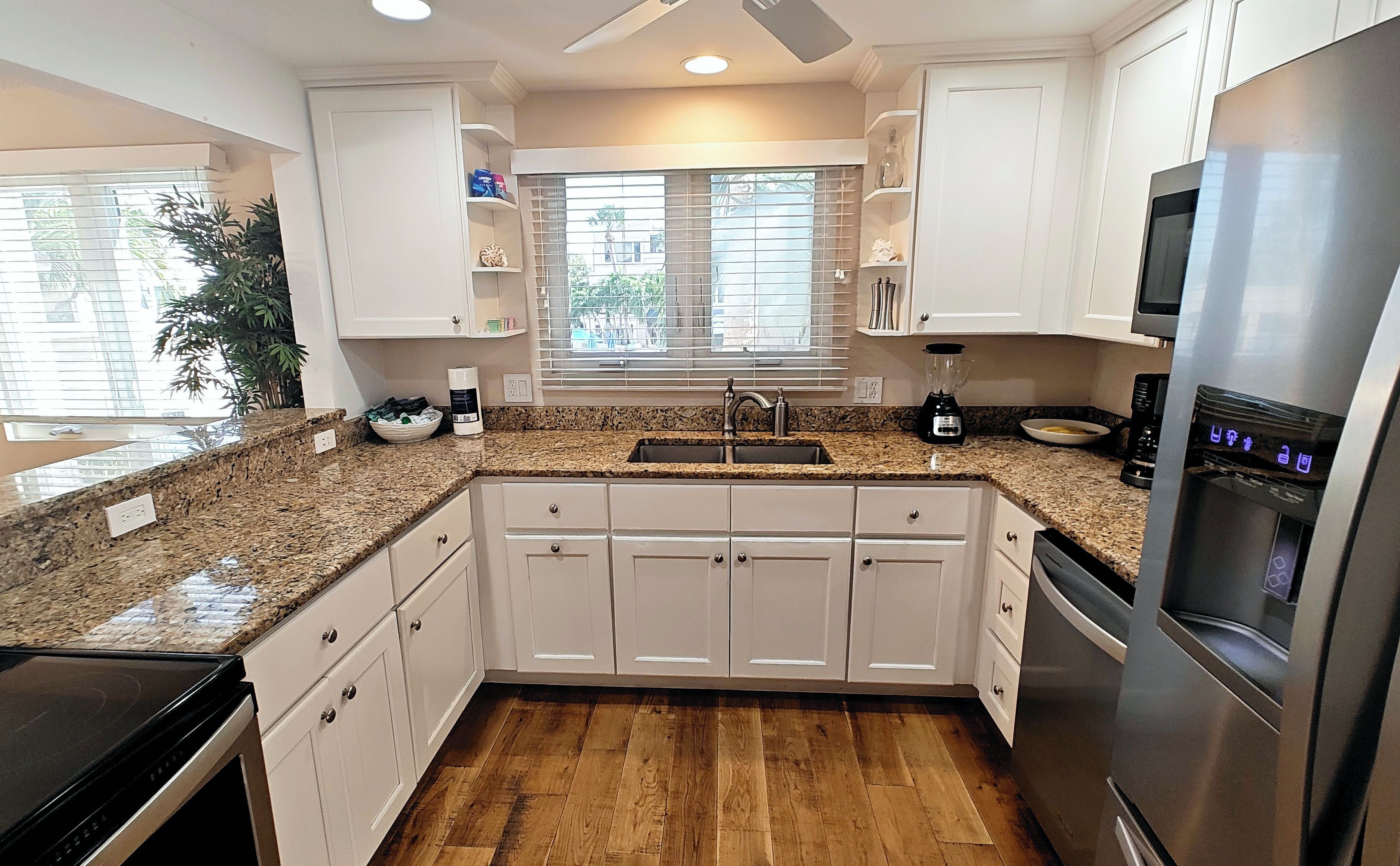 A kitchen with white cabinets, a granite countertop, a stainless steel refrigerator, and a window with blinds.