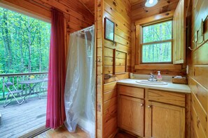 Une salle de bain rustique, aménagée dans une cabane en bois, avec une douche, un lavabo et une vue sur la forêt.