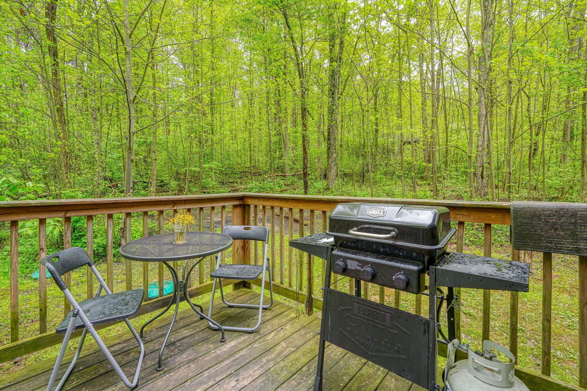 A wooden deck with a grill, two chairs, and a table.