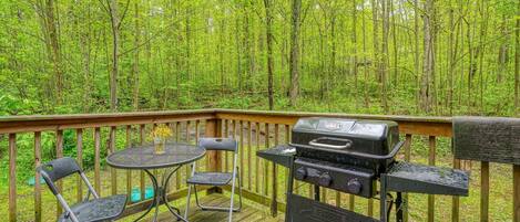 A wooden deck with a grill, two chairs, and a table.