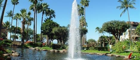 A fountain in a landscaped area with palm trees and a clear sky.