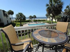 Une terrasse avec une table ronde et des chaises en osier, donnant sur une piscine et une plage.