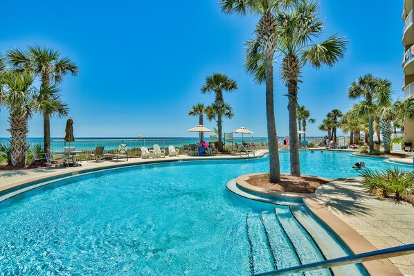 Relax by the oceanfront pool surrounded by palm trees and lounge chairs.
