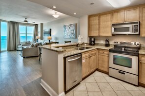 Enjoy ocean views from the large window in this apartment's spacious living area, featuring a comfortable sofa set.
