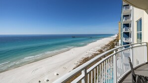 Une vue sur la plage depuis un balcon, avec un ciel dégagé, une plage de sable et une jetée qui s’avance dans l’eau.