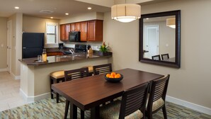 A modern kitchen with wooden cabinets, a black refrigerator, and a dining area with a wooden table and chairs. - Westin Desert Willow - 1 bedroom- Deluxe, Coachella 1st weekend - 820 sq ft (Palm Desert)