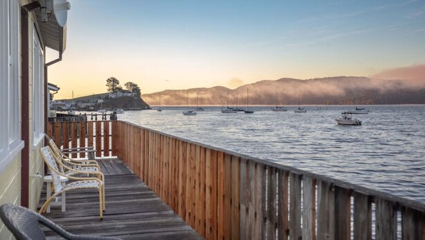 Eine Holzterrasse mit Stühlen, die auf ruhiges Wasser mit Booten blickt.