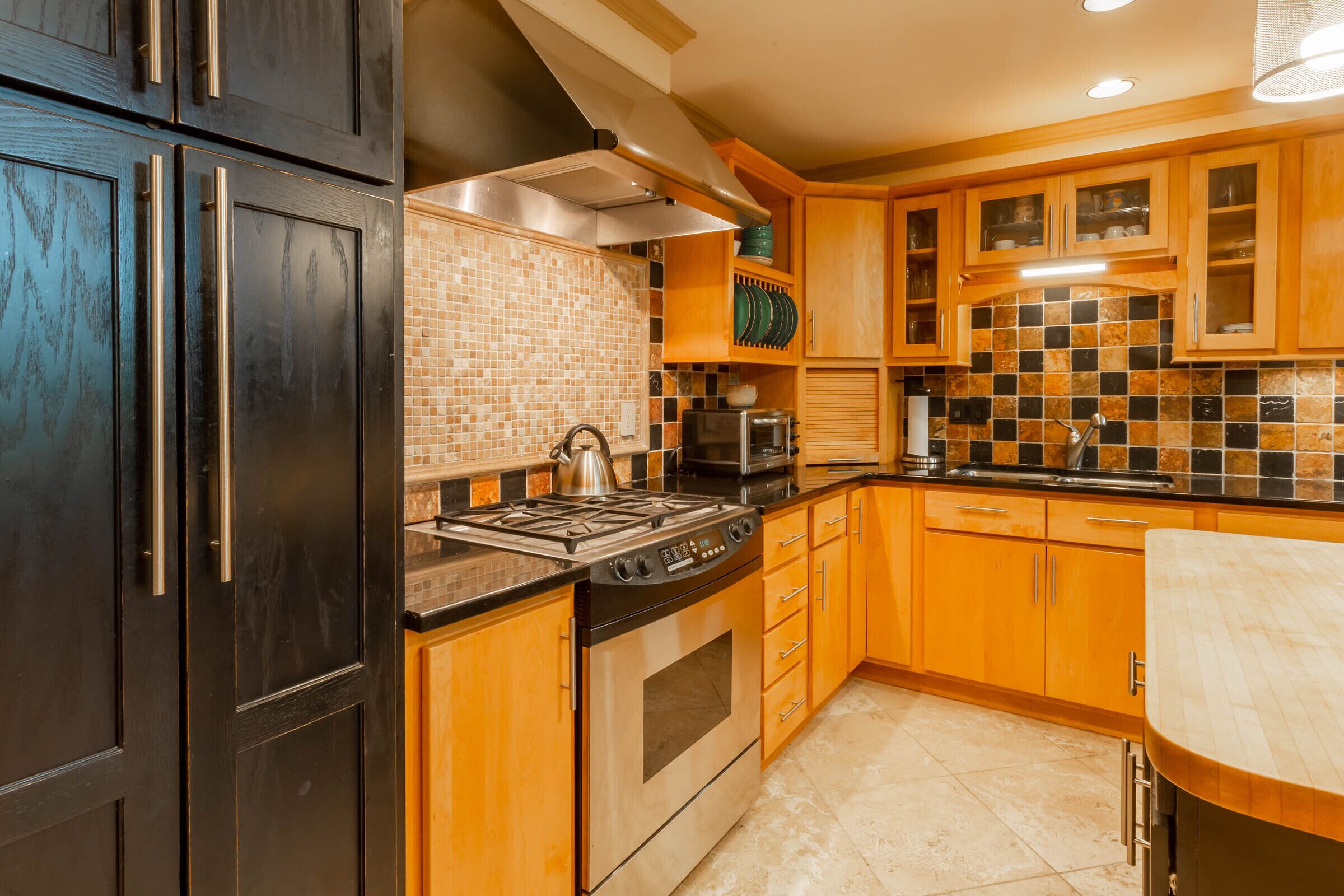 A kitchen with dark wooden cabinets, a tiled backsplash, stainless steel appliances, and wooden countertops.