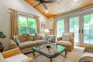 Un salon confortable avec un canapé, des fauteuils, une table basse en verre et un ventilateur de plafond.