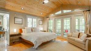 A spacious bedroom with a large bed, a sitting area with a sofa, and a view of the outdoors through large windows. - Beautiful 4BR Rehoboth Beach Home w/ Gorgeous Porch (Rehoboth Beach)