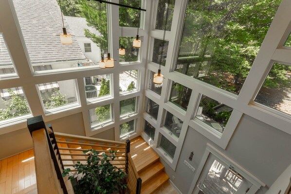 A multi-level interior with a wooden staircase, large windows, and hanging pendant lights.