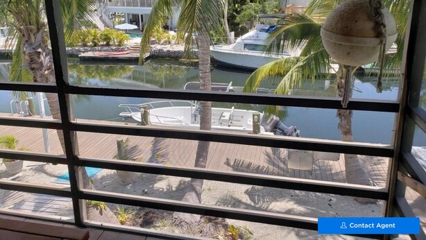 Blick aus einem Fenster auf eine Marina mit Booten, Palmen und einem Poolbereich.