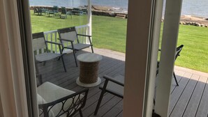 Une terrasse fermée par des moustiquaires, avec des sièges, une petite table et une vue sur l’océan.