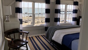 Une chambre avec un lit, une chaise et une vue sur la plage, grâce à de grandes fenêtres.