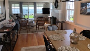 Un vaste espace de vie avec une grande fenêtre donnant sur la mer, une cheminée et une table à manger agrémentée de sets de table.