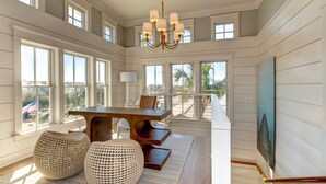 A spacious dining area with a wooden table and chairs, large windows, and a chandelier. - Luxury Ocean Blvd.  POOL/HOT TUB, PUTTING GREEN, ROOF TOP (Isle of Palms)
