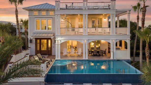 A two-story house with a large swimming pool, multiple balconies, and a well-lit interior. - Luxury Ocean Blvd.  POOL/HOT TUB, PUTTING GREEN, ROOF TOP (Isle of Palms)