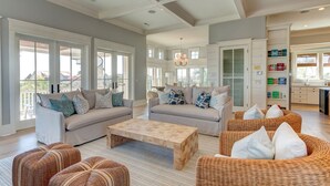 A spacious living room with a large sofa, a coffee table, and wicker furniture. There are large windows and a view of the outside. - Luxury Ocean Blvd.  POOL/HOT TUB, PUTTING GREEN, ROOF TOP (Isle of Palms)