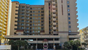 A multi-story hotel with a central entrance, balconies on each floor, and a clear sky above.