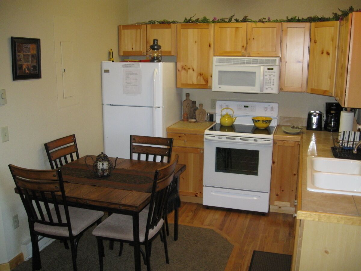 A kitchen with wooden cabinets, a white refrigerator, a microwave, an oven, and a dining table with chairs.