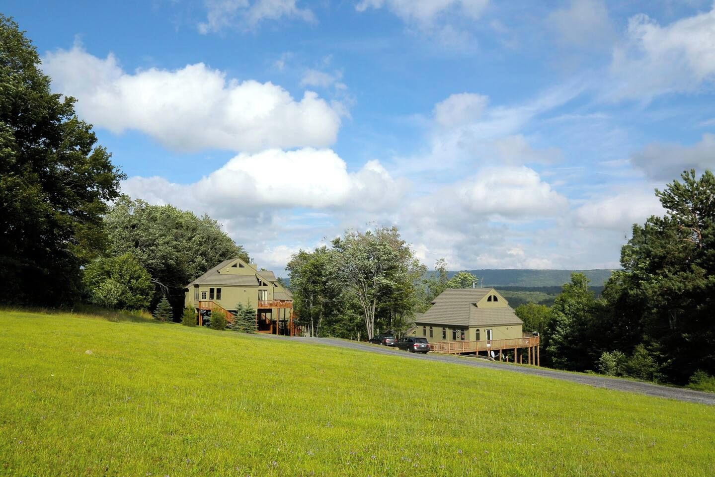 A two-story house with a porch and a small deck, surrounded by lush green grass and trees.