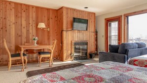 A cozy room with a wooden wall, a fireplace, a television, a sofa, and a bed.