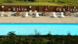A pool area with lounge chairs and umbrellas, surrounded by a wooden fence and a grassy field with mountains in the background. - Canaan Valley 1BR renovated 1BR, family friendly. (Davis)