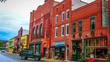 A street with red brick buildings, a green SUV parked on the side, and storefronts with various signs.