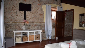 Een hotelkamer met een stenen muur, een witte console met manden, een bed met handdoeken en een aan de muur bevestigde televisie.