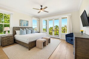 A bedroom with a bed, bedside tables, a ceiling fan, a TV, and large windows with a view. - Port of Call on Isle of Palms OCEAN FRONT, Pool, boardwalk, putting green (Isle of Palms)