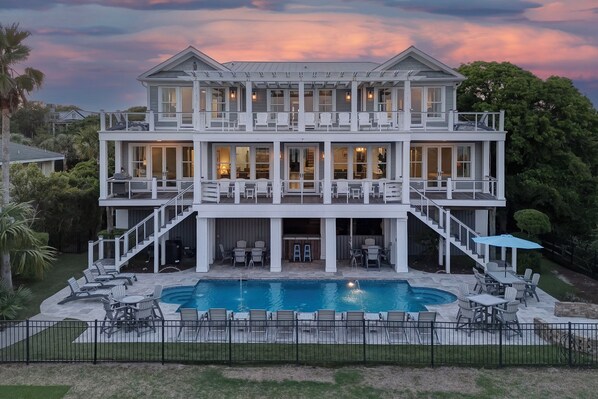 A two-story house with a large front porch, a swimming pool, and outdoor seating.