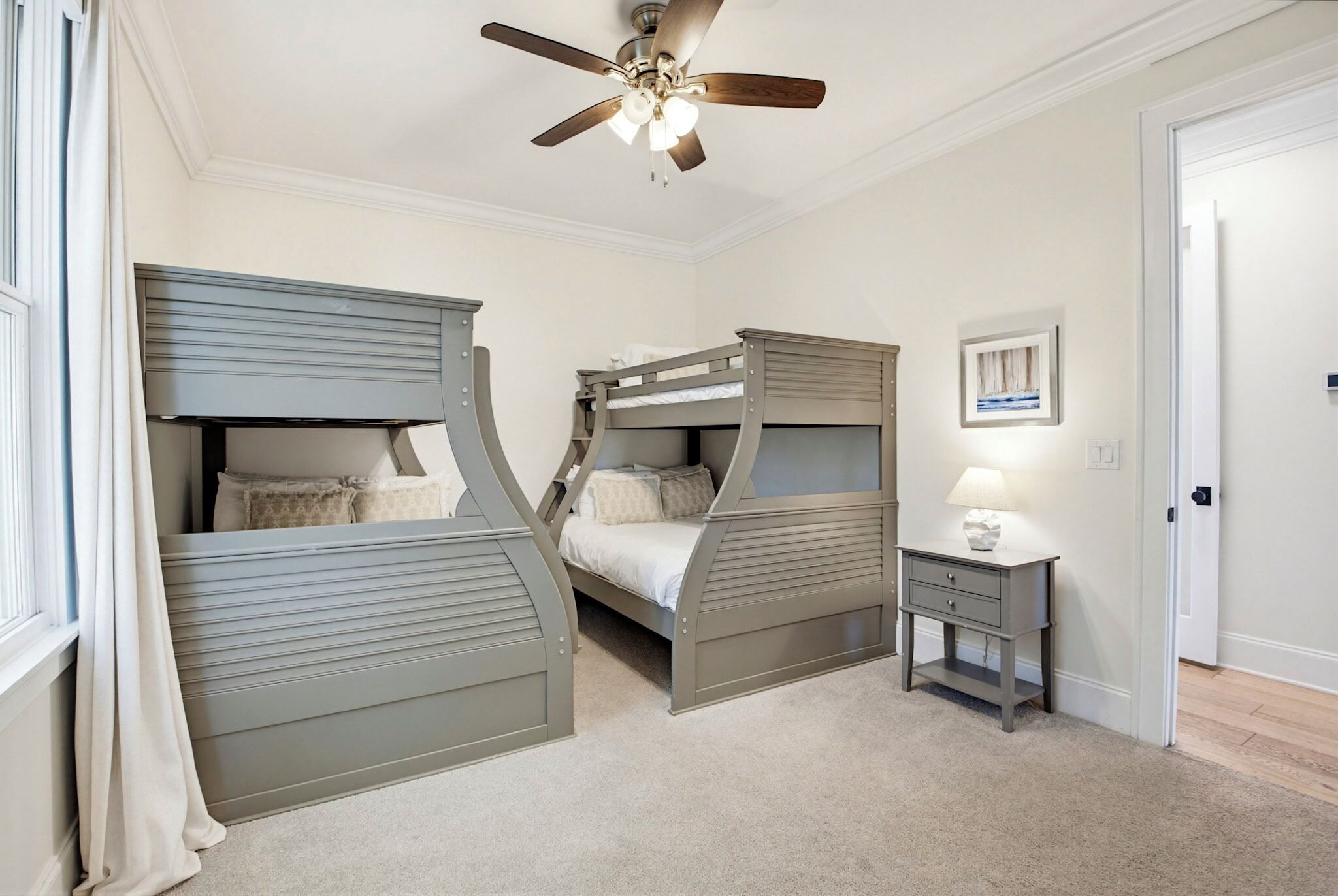 A bedroom with two bunk beds, a ceiling fan, a bedside table with a lamp, and a framed picture on the wall.