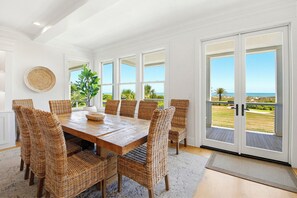 A dining area with a wooden table and wicker chairs, large windows with a view of the outdoors, and a balcony with a view of the ocean. - Port of Call on Isle of Palms OCEAN FRONT, Pool, boardwalk, putting green (Isle of Palms)