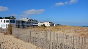 Une propriété située en bord de mer, dotée d’une clôture en bois, d’un bâtiment blanc et offrant une vue sur l’océan.