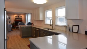 Une cuisine moderne dotée d’un grand îlot central, de meubles de couleur sombre et d’une fenêtre avec des stores.