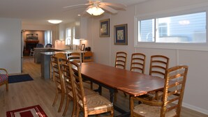 Un coin repas avec une table et des chaises en bois, un ventilateur de plafond et une vue sur l’extérieur par une fenêtre.