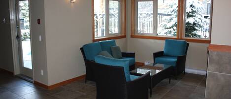 A room with two blue sofas, a small table, and large windows with a view of snow-covered trees.