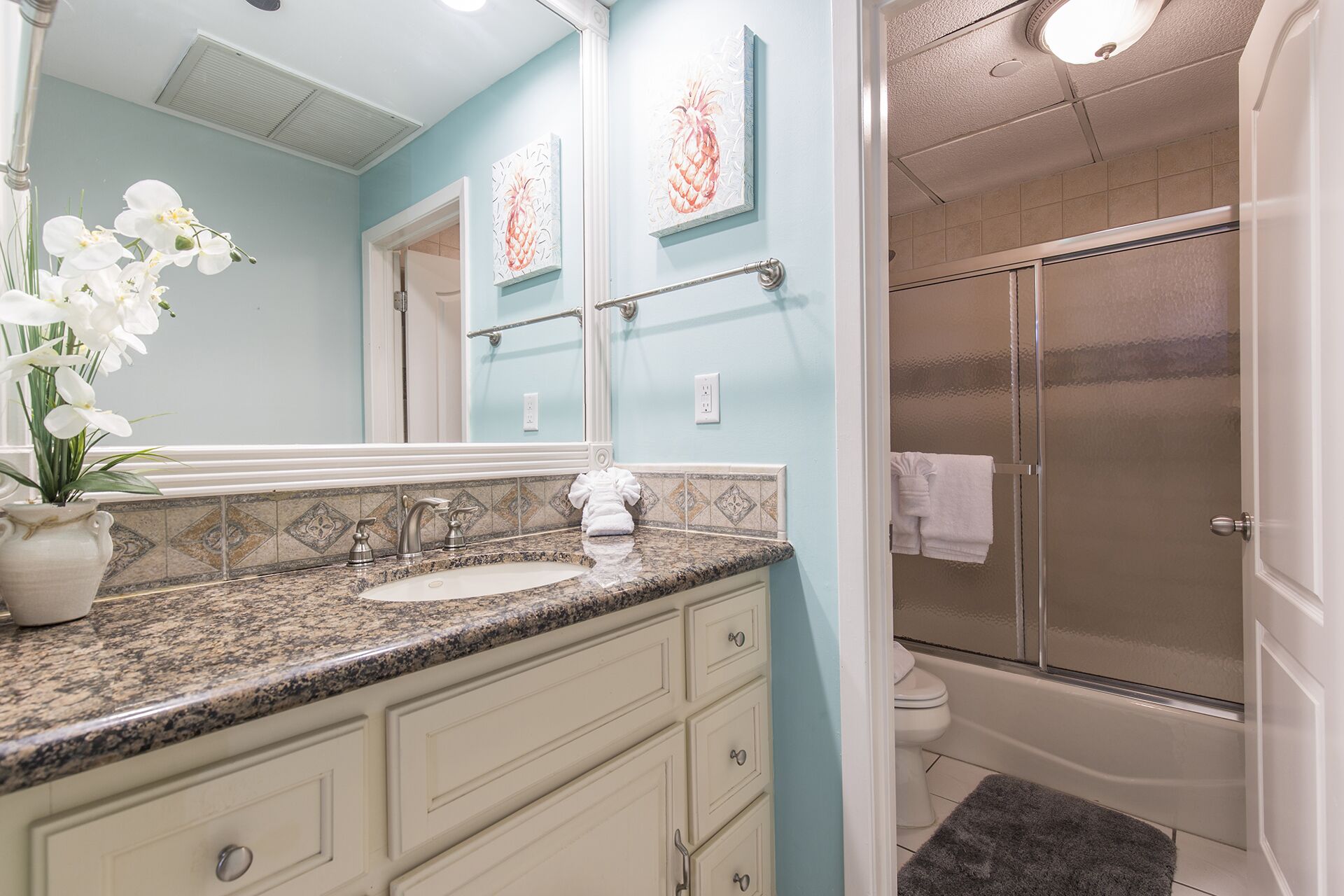 A bathroom with a granite countertop, white sink, and a glass shower enclosure.