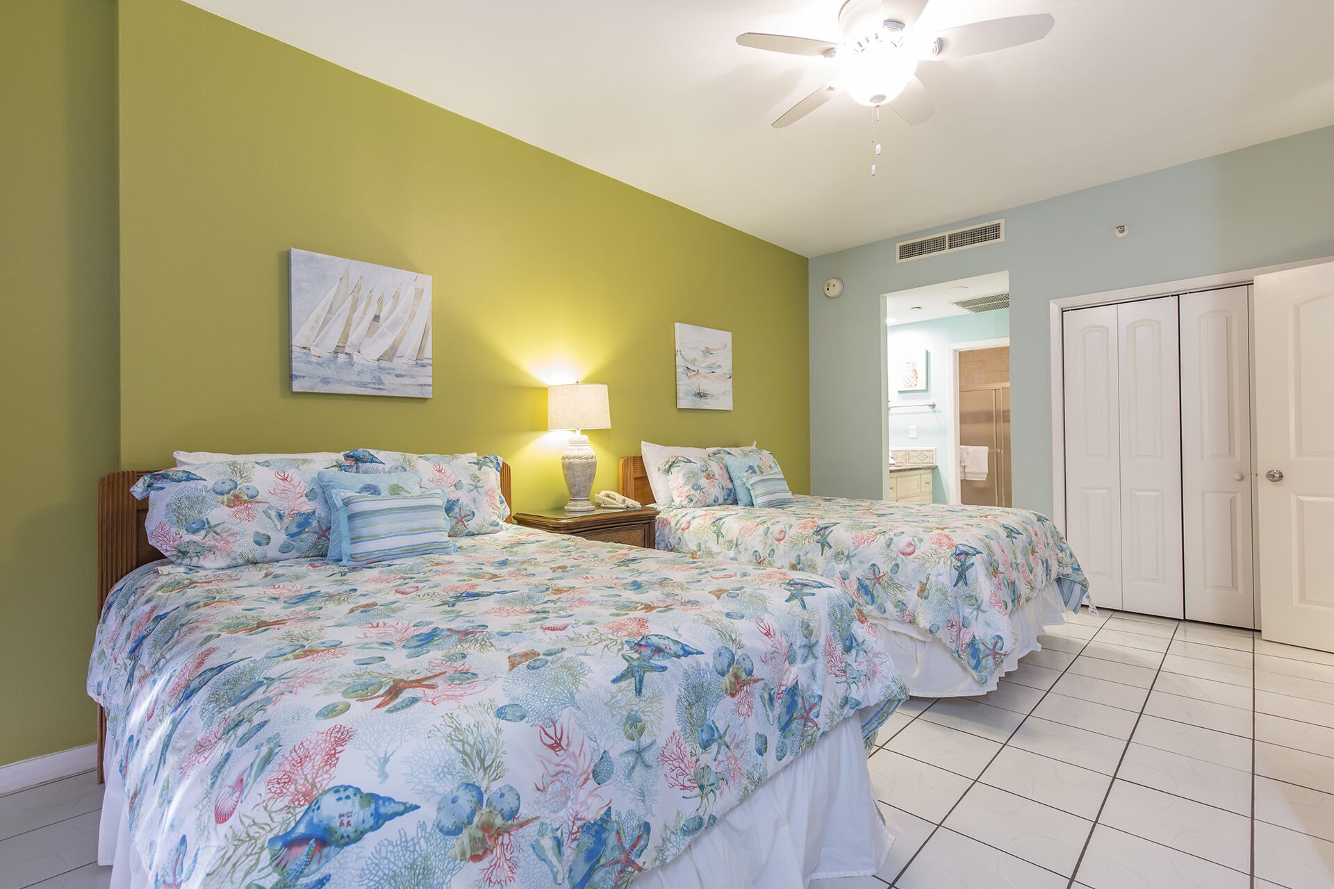 A bedroom with two beds, a ceiling fan, and artwork on the walls.