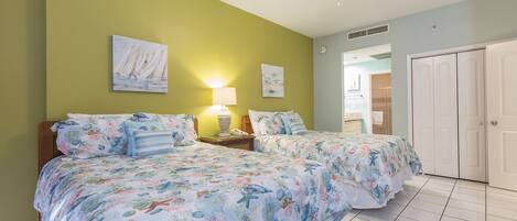 A bedroom with two beds, a ceiling fan, and artwork on the walls.