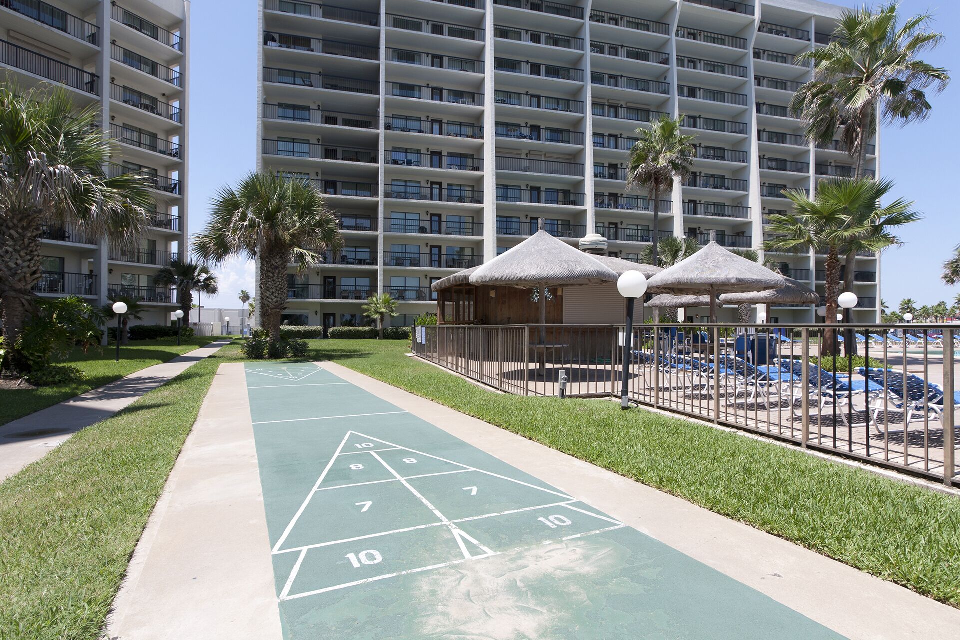 A hotel with a large building, a shuffleboard court, and a pool area with umbrellas.