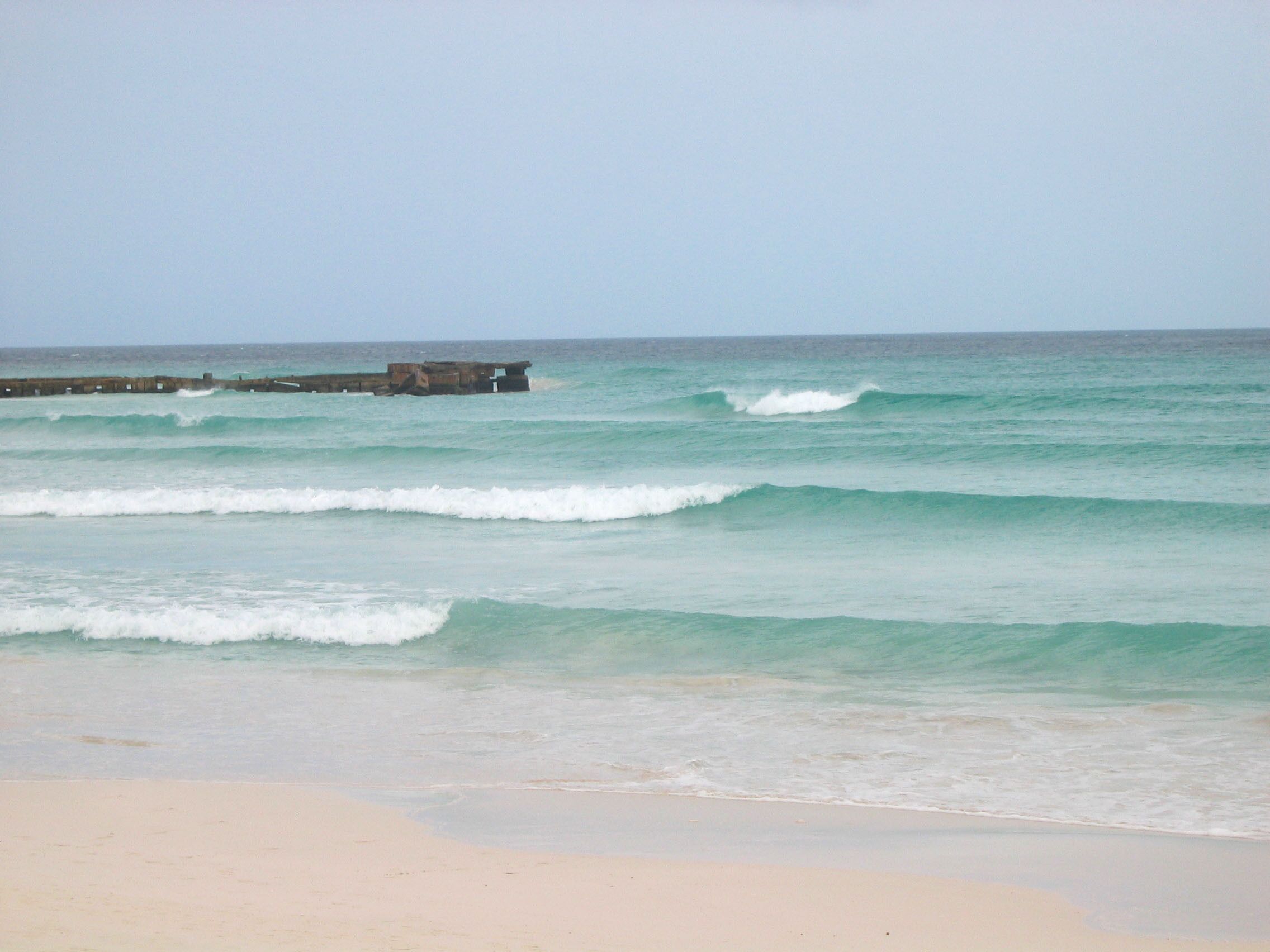A beach with waves and a pier in the distance.