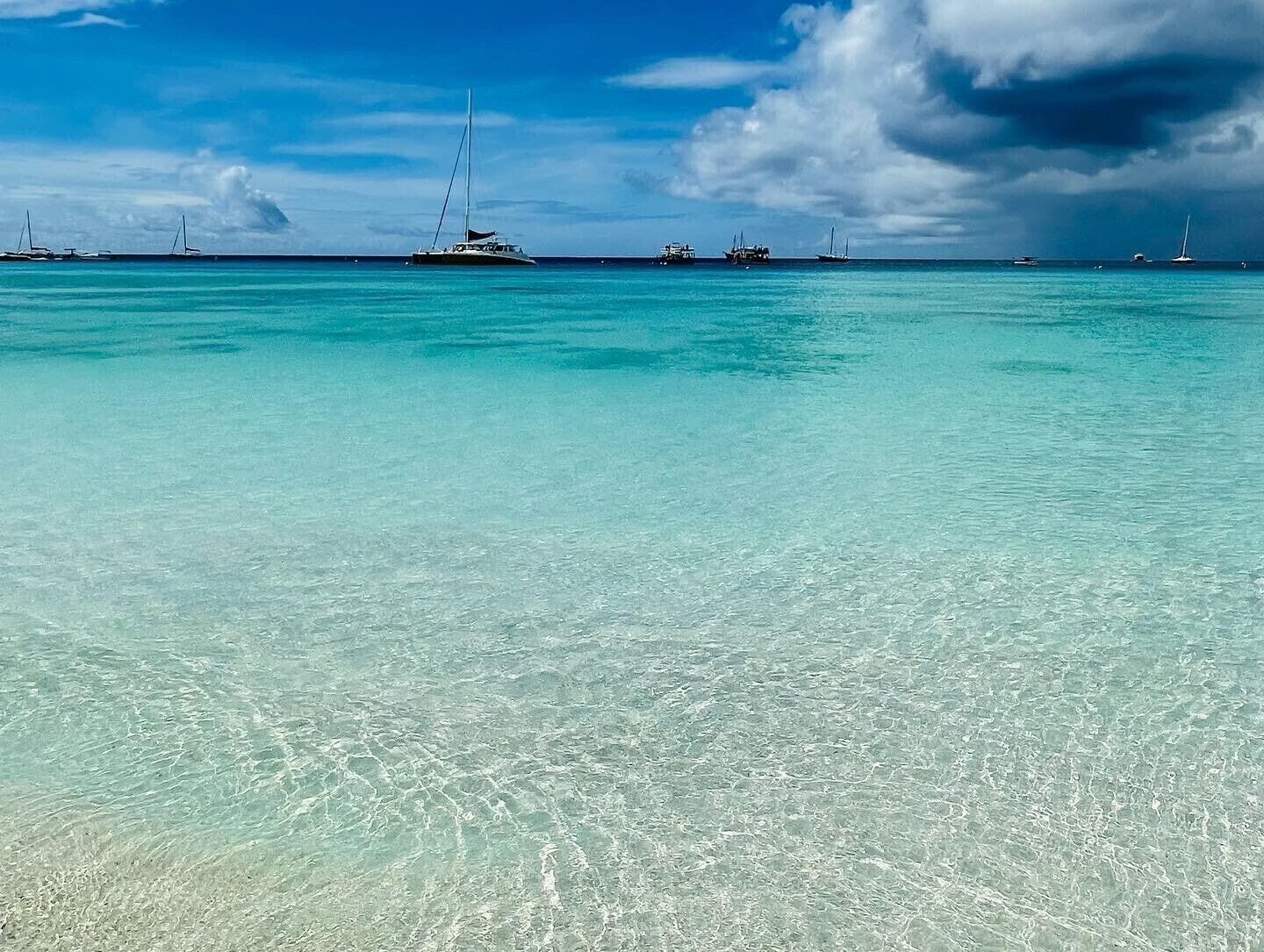A clear turquoise sea with several boats anchored in the distance.