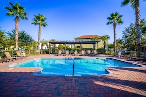 A swimming pool with lounge chairs and palm trees, surrounded by a brick patio.