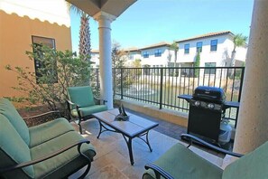 A patio area with green chairs, a table, and a barbecue grill.