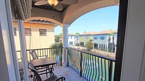 Un balcon avec une table et des chaises, une vue sur une piscine et, au loin, un quartier résidentiel.